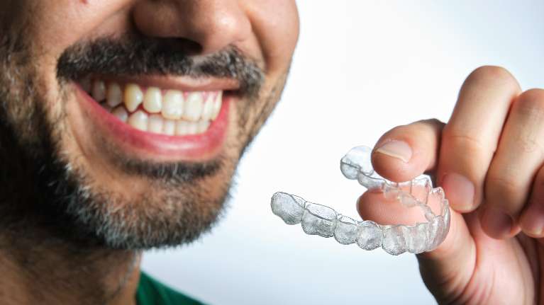 dental patient holding clear plastic aligner | family dentist near me